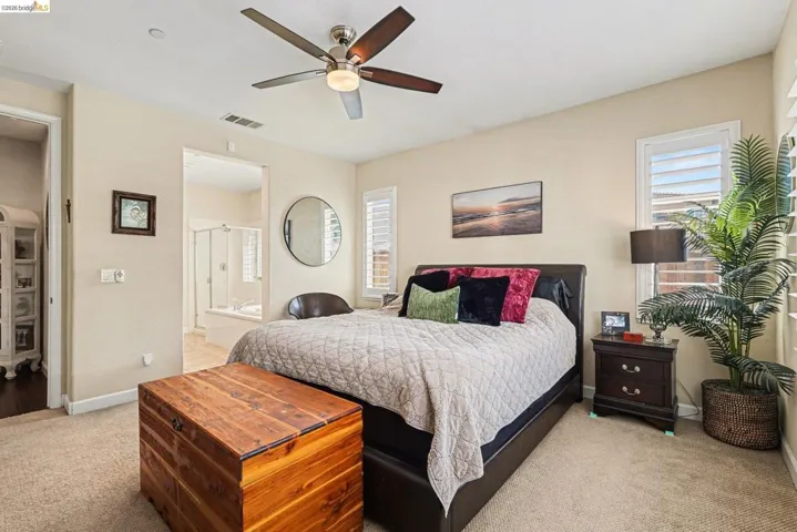 Bedroom featuring light carpet, a ceiling fan, multiple windows, and connected bathroom