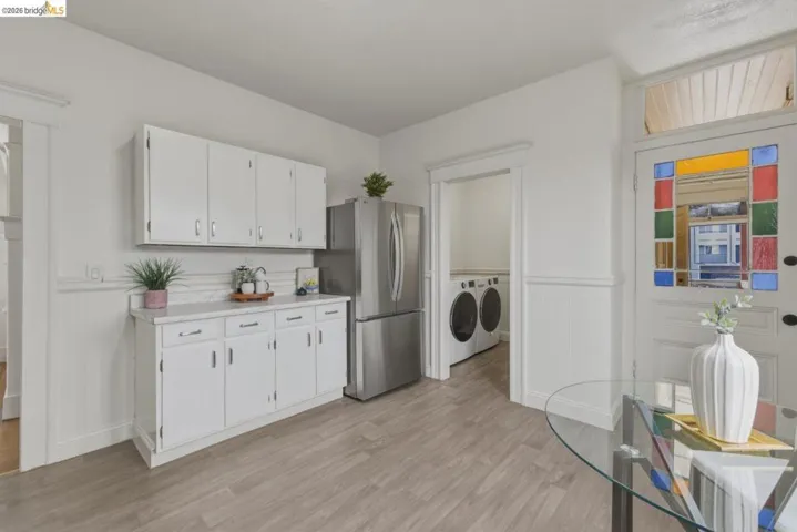 Kitchen with white cabinetry, light countertops, a wainscoted wall, washing machine and clothes dryer, and light wood-style flooring