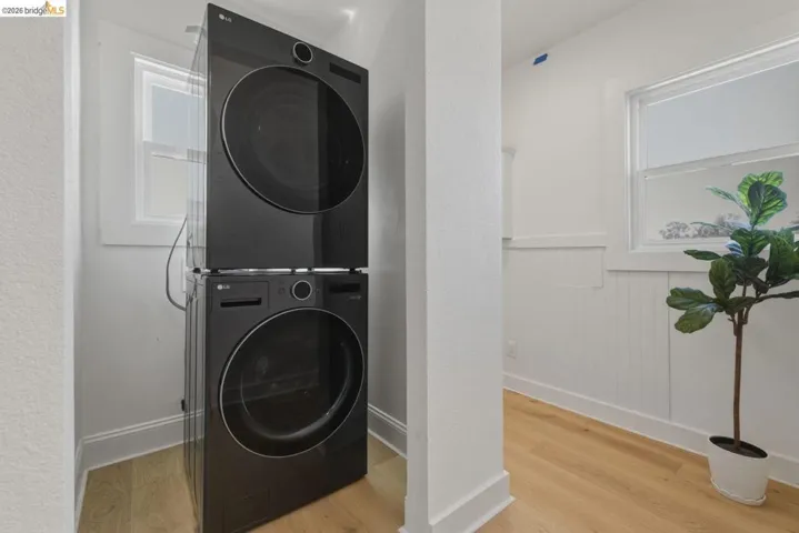 Laundry area with a wainscoted wall, stacked washer and clothes dryer, and light wood-style flooring