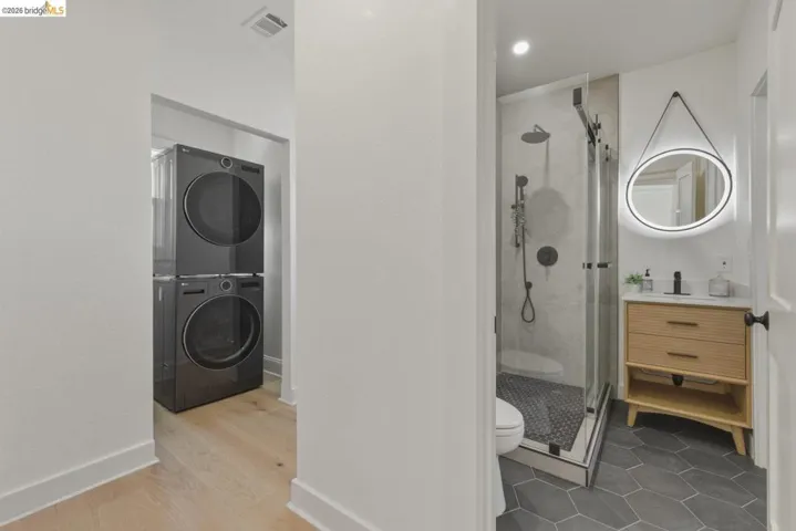 Bathroom with a shower stall, vanity, stacked washer and dryer, and light wood-type flooring