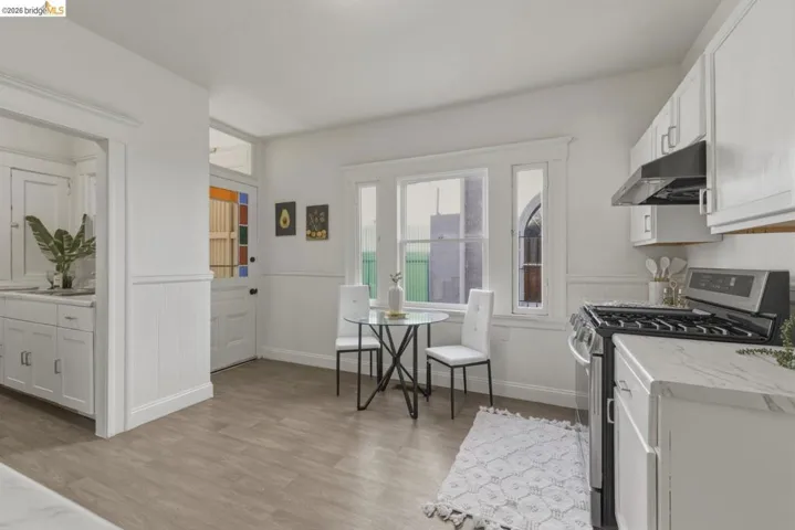 Kitchen with stainless steel gas range, white cabinetry, light wood finished floors, wainscoting, and light stone counters
