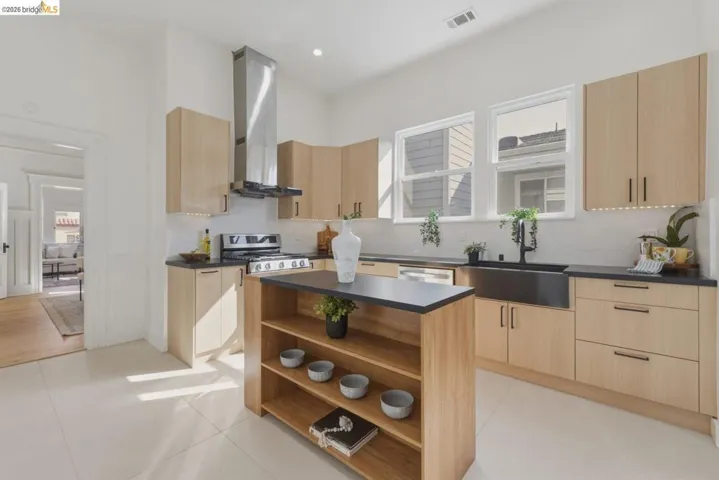 Kitchen featuring light wood finish cabinets, open shelves, dark countertops, ventilation hood, and a kitchen island