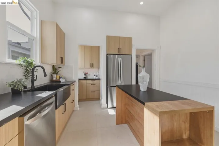 Kitchen with stainless steel appliances, light wood finish cabinetry, dark countertops, modern cabinets, and wainscoting