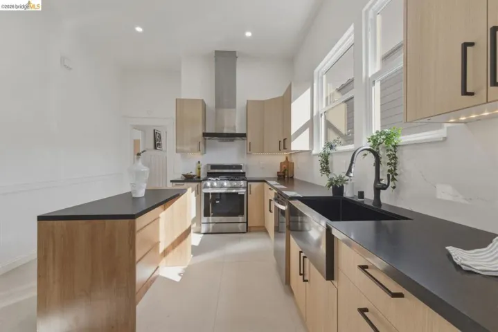 Kitchen with light wood finish cabinets, dark countertops, stainless steel appliances, a wainscoted wall, and recessed lighting