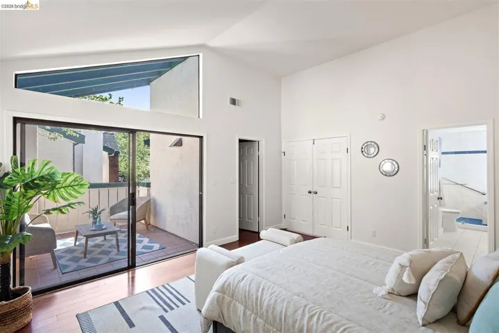Bedroom featuring lofted ceiling, wood finished floors, access to outside, ensuite bathroom, and a closet