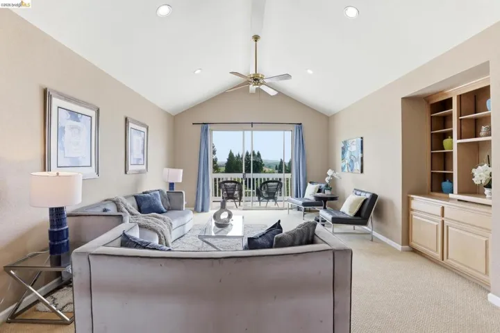 Living area featuring light carpet, a ceiling fan, and beamed ceiling