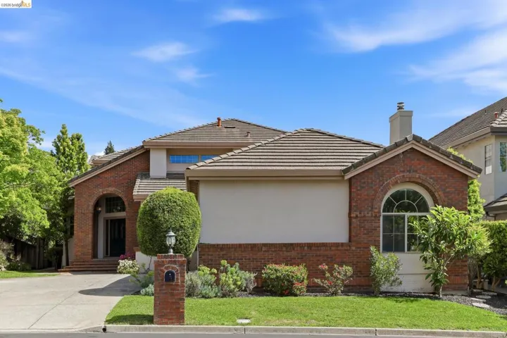 View of front of property with brick siding, a front lawn, a chimney, and a tiled roof