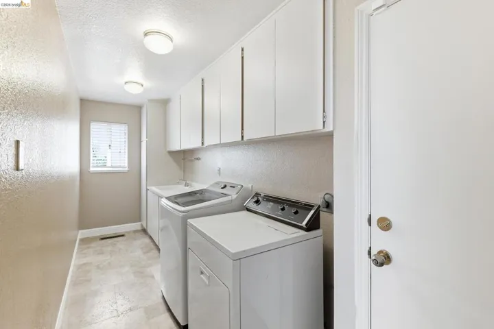 Laundry area with a textured wall, a textured ceiling, cabinet space, and washing machine and clothes dryer