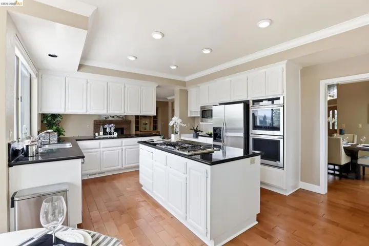 Kitchen featuring white cabinetry, stainless steel appliances, a kitchen island, light wood finished floors, and ornamental molding