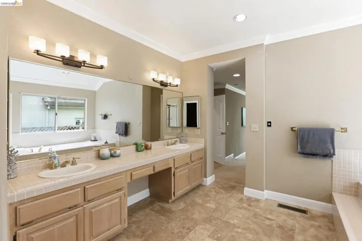 Bathroom featuring a bath, double vanity, crown molding, and recessed lighting
