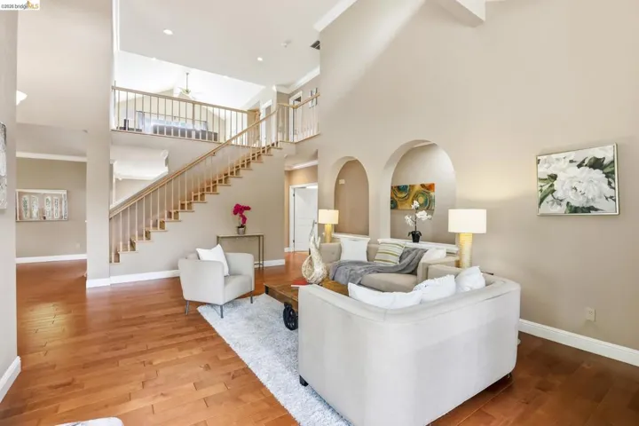 Living area featuring ornamental molding, a high ceiling, wood-type flooring, a ceiling fan, and arched walkways