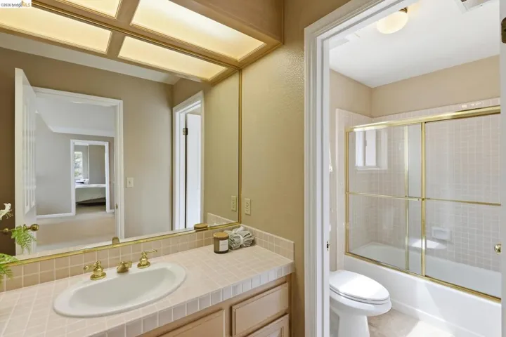 Full bath with shower / bath combination with glass door, vanity, and a textured wall