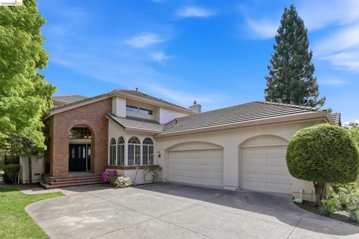 Traditional home featuring a tiled roof, a garage, stucco siding, concrete driveway, and brick siding