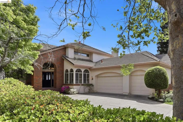 Traditional-style house featuring a garage, stucco siding, a tile roof, brick siding, and driveway