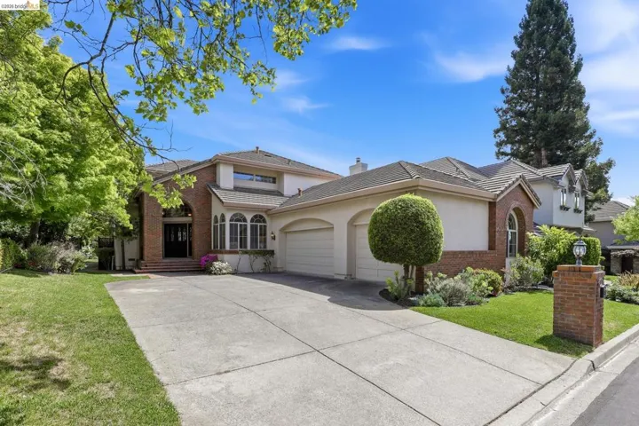 Traditional-style home featuring an attached garage, brick siding, a front yard, stucco siding, and a tiled roof