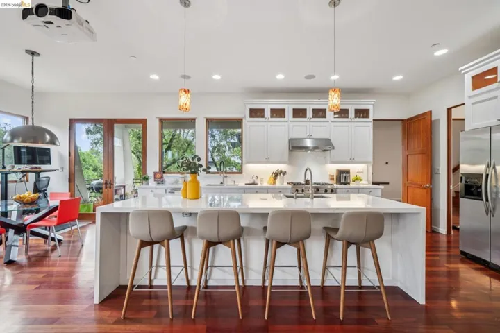 Kitchen with light stone counters, white cabinets, a large island with sink, and a kitchen breakfast bar