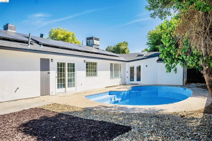 Rear view of house with french doors, roof mounted solar panels, roof with shingles, an outdoor pool, and a patio