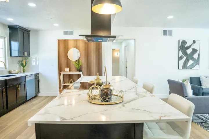 Kitchen with light stone counters, light wood-style floors, island exhaust hood, recessed lighting, and a kitchen bar