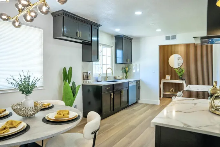 Kitchen featuring exhaust hood, light wood finished floors, stainless steel dishwasher, decorative backsplash, and light stone countertops