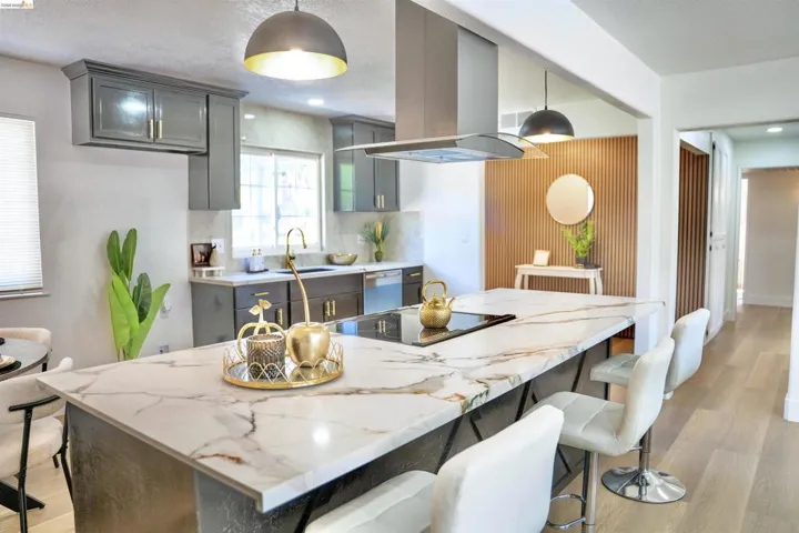 Kitchen with light wood-style flooring, a breakfast bar area, island exhaust hood, light stone counters, and a textured ceiling