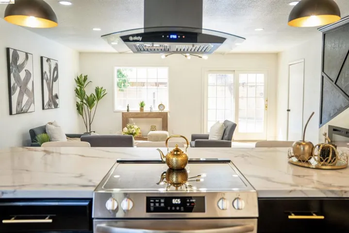 Kitchen with open floor plan, island range hood, light stone countertops, stainless steel electric range oven, and recessed lighting