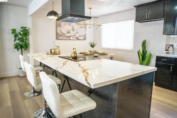 Kitchen featuring a breakfast bar area, light wood-style floors, island exhaust hood, dark cabinetry, and light stone countertops