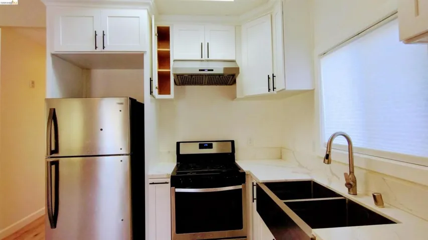 Kitchen featuring stainless steel appliances, white cabinetry, and light stone counters
