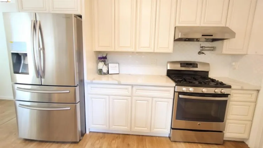 Kitchen featuring stainless steel appliances, light stone countertops, light wood finished floors, white cabinets, and tasteful backsplash