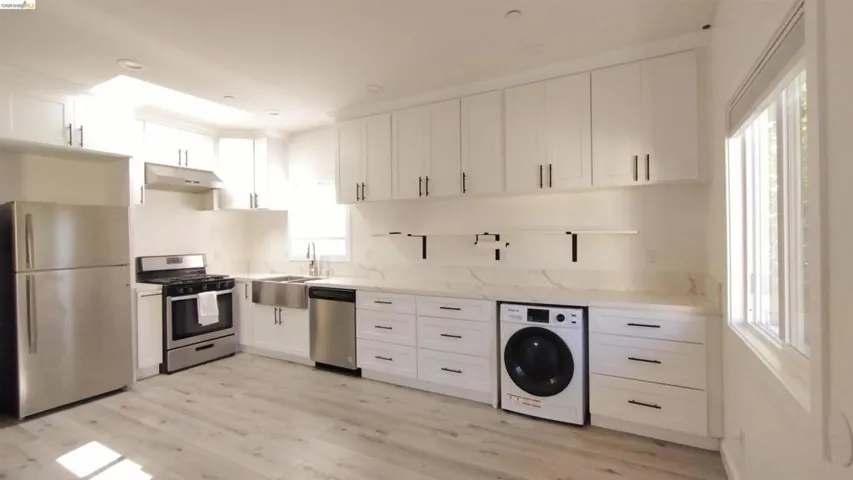 Kitchen featuring white cabinets, stainless steel appliances, washer / clothes dryer, and light wood finished floors
