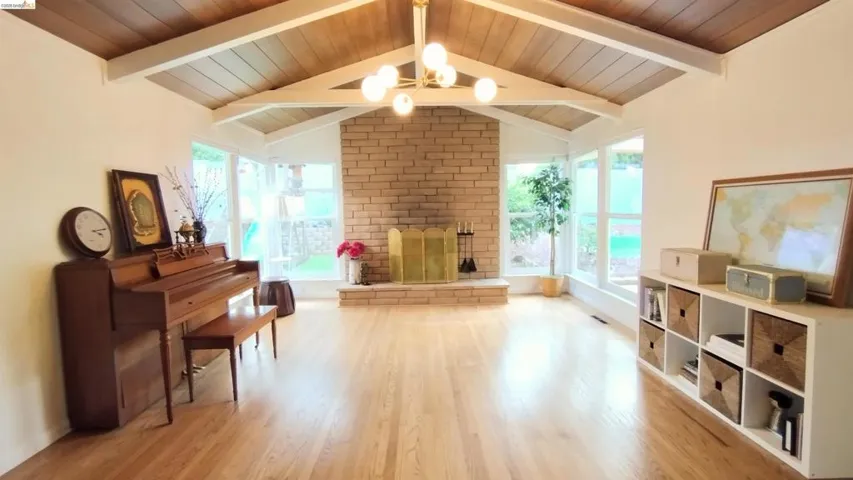 Sitting room with light wood-type flooring, a brick fireplace, and a wood ceiling with exposed beams