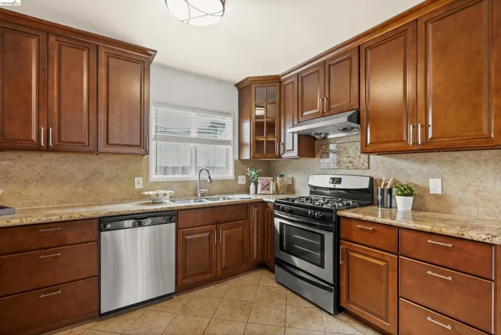 Kitchen with stainless steel appliances, light stone counters, glass fronted cabinets, and light tile patterned floors