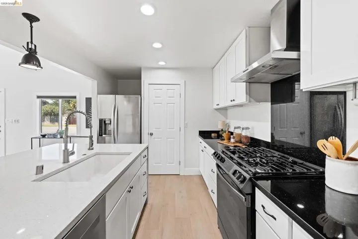 Kitchen featuring stainless steel appliances, white cabinetry, dark stone counters, light wood-type flooring, and hanging light fixtures
