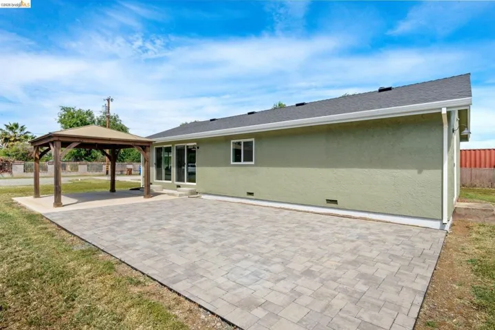 Rear view of property featuring a patio area, a gazebo, stucco siding, roof with shingles, and crawl space