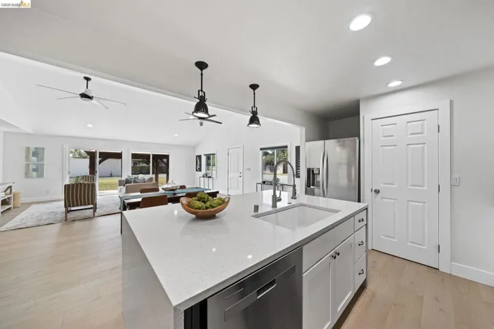 Kitchen featuring light stone countertops, stainless steel appliances, light wood-style floors, open floor plan, and an island with sink