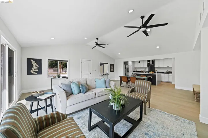 Living room with light wood finished floors, a ceiling fan, vaulted ceiling, and recessed lighting