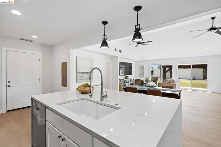 Kitchen featuring light wood-style floors, light stone counters, vaulted ceiling, decorative light fixtures, and stainless steel dishwasher