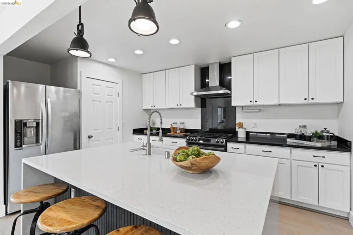 Kitchen featuring dark stone countertops, stainless steel appliances, white cabinets, and a kitchen bar