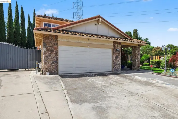 View of front of house featuring stone siding, driveway, an attached garage, and stucco siding with side yard access and second detached 2 car metal garage.