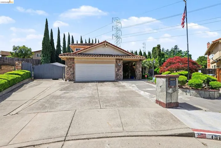 View of front facade with stone siding, concrete driveway, a gate, tiled roof with 3+ car driveway, side yard and 2 car detached metal garage