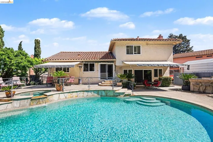 Back of property with a patio area, stucco siding, a chimney, a pool with connected hot tub, and a tile roof
