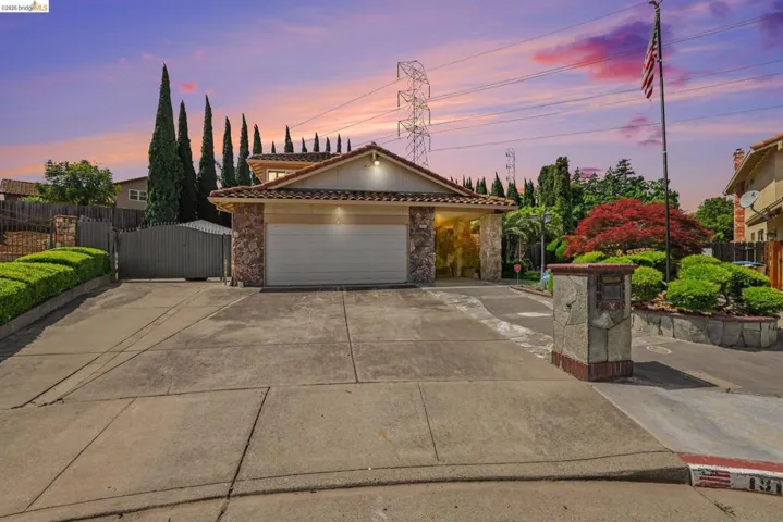 View of front facade featuring stone siding, driveway, a gate, a tiled roof, and a 2-car garage