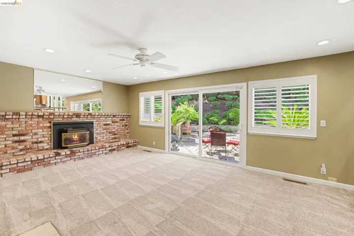 Family room with ceiling fan, recessed lighting, new carpet, and a brick fireplace with gas insert.