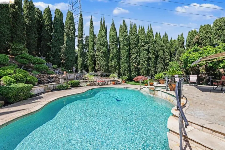 Combined pool / hot tub featuring a patio and view of scattered trees