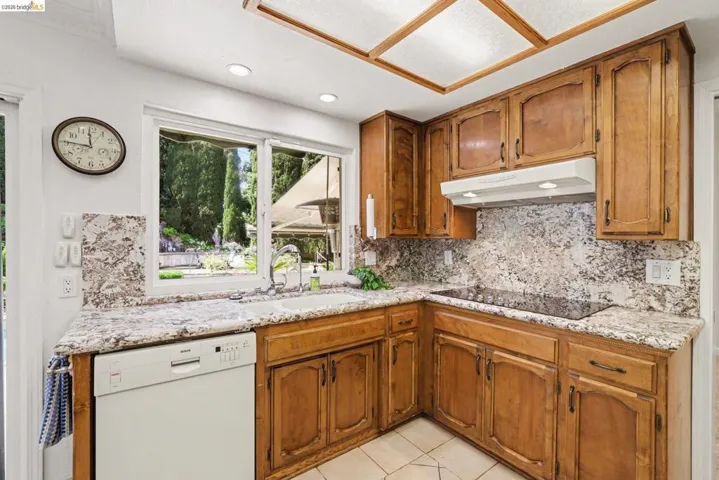 Kitchen with dishwasher, wood finish cabinetry, granite counters and backslash, recessed lighting, ceiling fan, built in oven, microwave and pull out drawers.