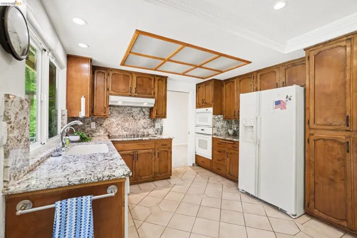 Kitchen with wood finish cabinets, granite countertops and backsplash, white appliances, tasteful backsplash, and recessed lighting and pantry