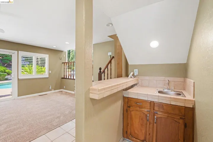 Bar area featuring wood finish cabinetry, tile counters, carpet and lofted ceiling.