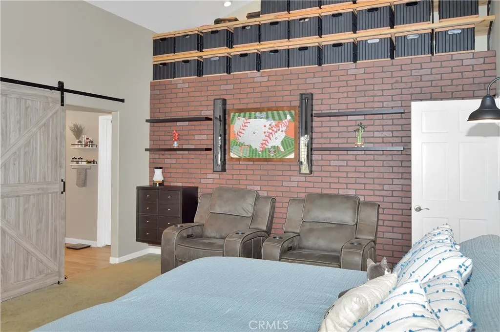 The spacious main bedroom suite boasts more custom built-ins with another heated fireplace and display shelves surrounding the TV (which is included and on a swivel mount for viewing from bed, too), a matching lighted headboard (included), brick accent wall with cabinet and shelving, dramatic cathedral ceilings, louvered shutters, a fantastic fan, and a barn door leading to the en suite bath.