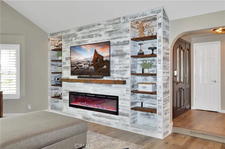 The living room is right next to the entry and features a stunning, custom built-in with heated fireplace, mantel, and display shelves, along with pet-friendly flooring, an impressive ceiling fan, and louvered shutters. The TV and extra-long couch are both negotiable. (TV image added virtually)