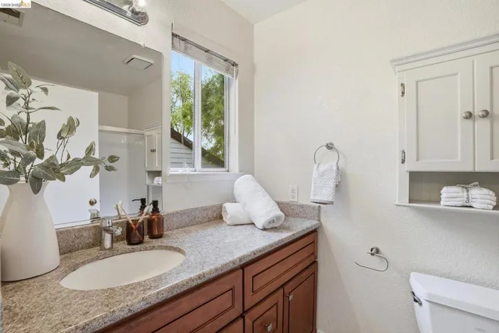 Bathroom featuring a granite-style countertop with an integrated sink, rich wood-finish cabinetry, built-in wall cabinet with open shelving, and a bright window