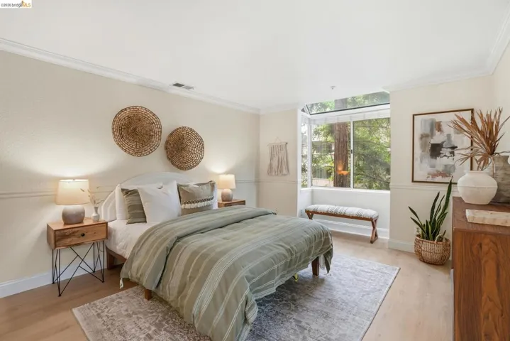 Room featuring multiple large windows, light wood-finish flooring, a bright ceiling, crown molding, and wainscoting